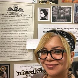 A woman in glasses smiles at the camera; behind her a door bears different pictures of Chicanx and women's history.